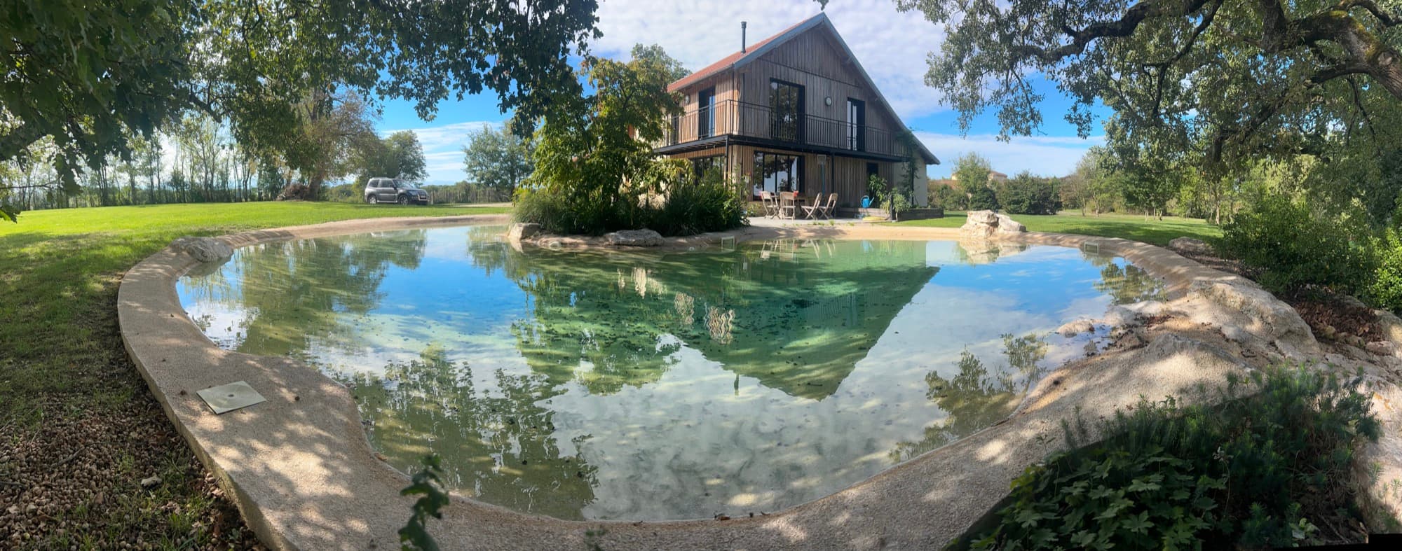 Bassin de baignade naturelle reflétant une grange, en bord de prairie
